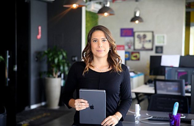 Mulher profissional em escritório, segurando tablet e olhando para frente.
