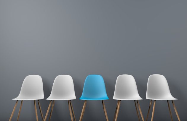 Cinco cadeiras alinhadas: uma azul central e quatro brancas. Parede cinza.