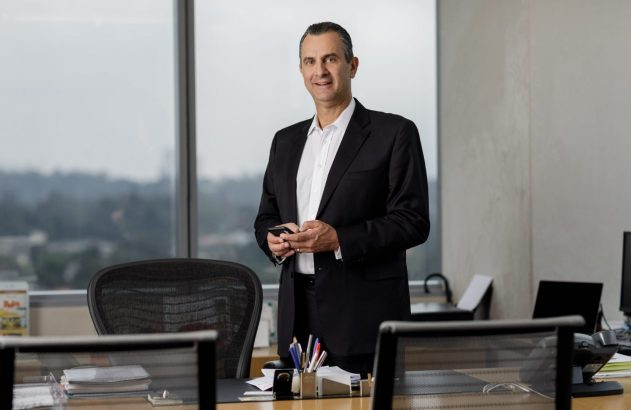 Executivo em pé em seu escritório, com janela e vista, olhando para frente.