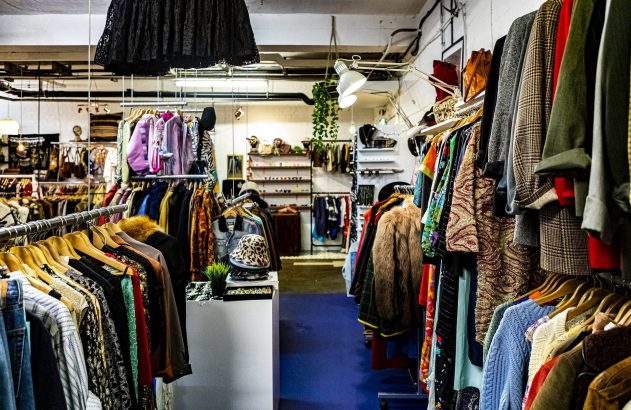 Interior de brechó com araras de roupas vintage coloridas, casacos e acessórios.