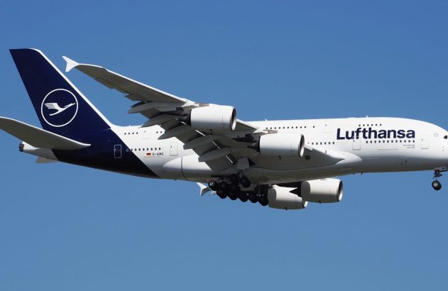 Airbus A380 da Lufthansa em voo com trem de pouso abaixado no céu azul.