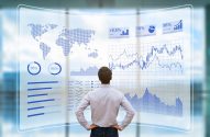Um homem de costas observa uma tela digital transparente exibindo gráficos de desempenho e dados financeiros globais.