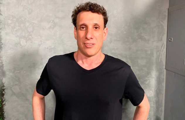 Homem adulto de camisa preta em pé, olhando para a câmera.