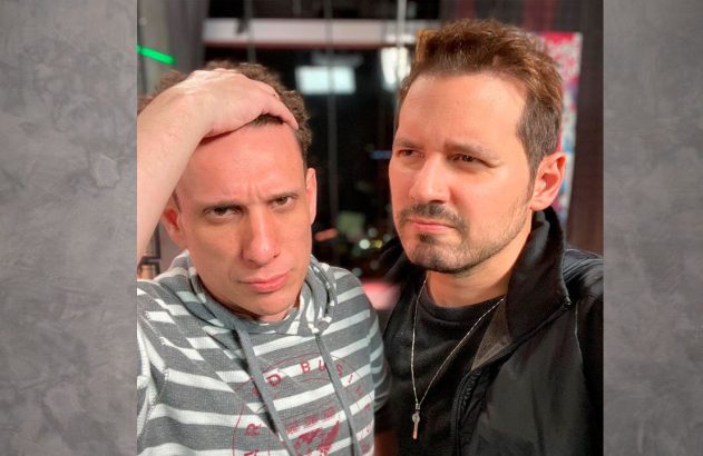 Dois homens, um com a mão na cabeça, posam para selfie com expressão séria.