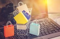 Sacolas de compras e carrinho em miniatura no teclado de um notebook, representando e-commerce.