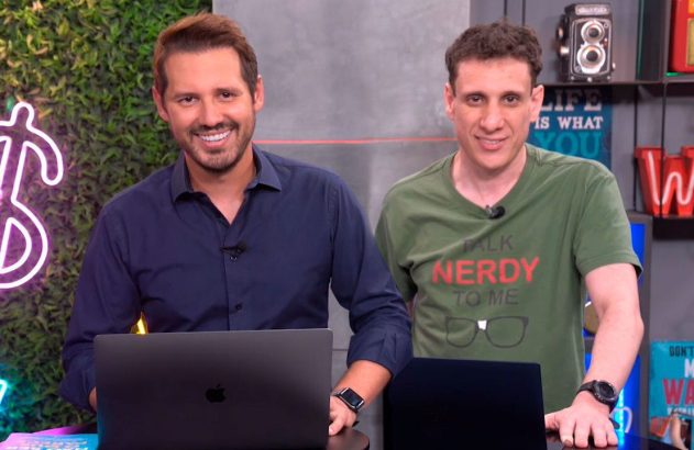 Dois homens sorridentes, com laptops, em um estúdio. Um veste camiseta "Talk Nerdy To Me".