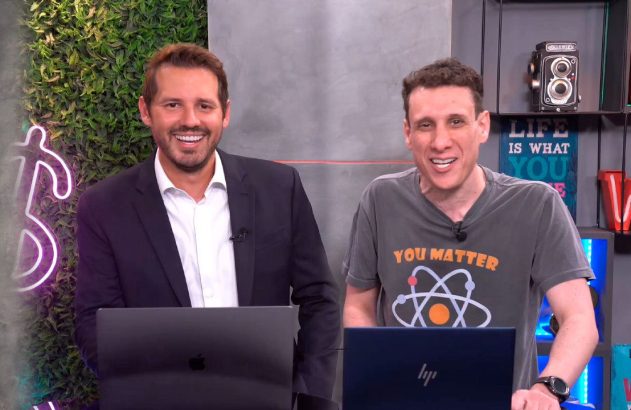 Dois homens sorrindo, com notebooks, em ambiente de gravação.