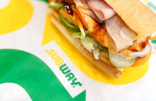 Sanduíche Subway aberto em embalagem com logo da marca. Exibe recheio de carne e vegetais.