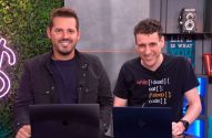Dois homens sorridentes em um estúdio, sentados em frente a laptops.