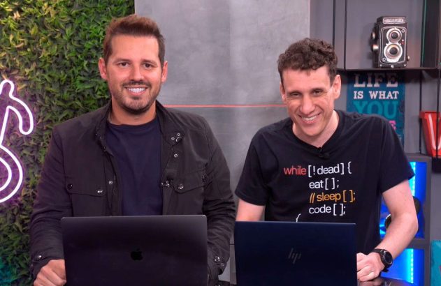 Dois homens sorridentes em um estúdio, sentados em frente a laptops.