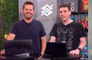 Dois homens sorrindo em estúdio com laptops, um logo e parede de folhagens. Eles olham para a câmera.