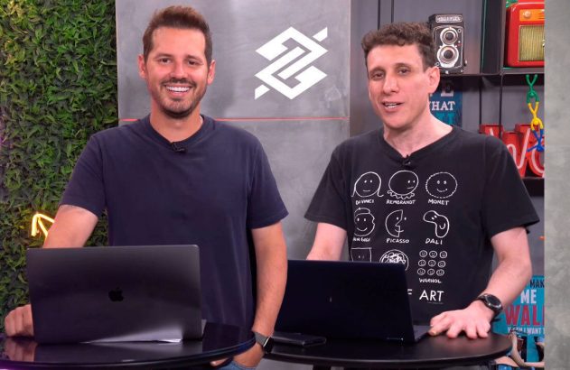 Dois homens sorrindo em estúdio com laptops, um logo e parede de folhagens. Eles olham para a câmera.