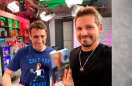 Dois homens sorrindo em estúdio. O da direita segura um livro e o da esquerda veste uma camiseta "CALC YOU LATER!".