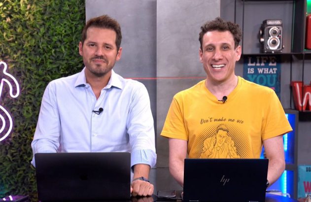 Dois homens sorrindo para a câmera, sentados em estúdio com laptops e fundo decorado.
