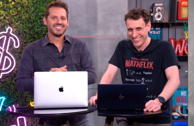 Dois homens sorridentes atrás de laptops (um MacBook) em estúdio com iluminação neon ao fundo.