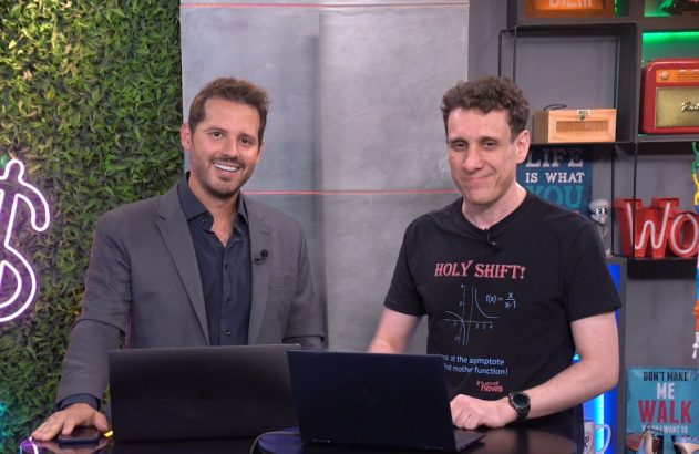 Dois homens sorridentes em um estúdio, em pé com laptops à frente, olhando para a câmera.