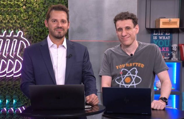 Dois homens sorrindo para a câmera em estúdio, com laptops à frente e decorações ao fundo.
