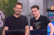 Dois homens sorrindo posam com laptops em um estúdio.