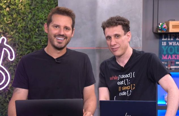 Dois homens sorrindo posam com laptops em um estúdio.