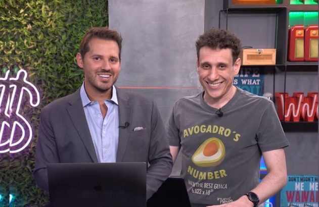 Dois homens sorrindo para a câmera em estúdio. Um usa blazer e o outro camiseta.