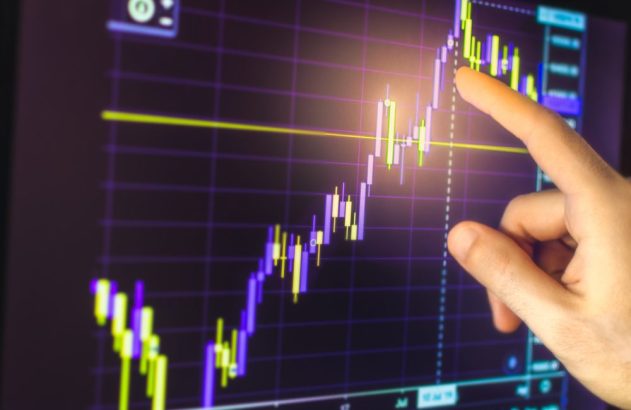 Mão apontando para gráfico financeiro em tela, mostrando tendência de alta.