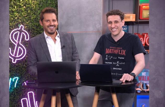 Dois homens sorridentes, um de terno e outro com camiseta 'MATHFLIX', atrás de laptops em um cenário.