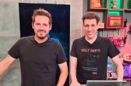 Dois homens em camisetas pretas posam lado a lado em um estúdio. Um deles tem barba, o outro cabelo cacheado.