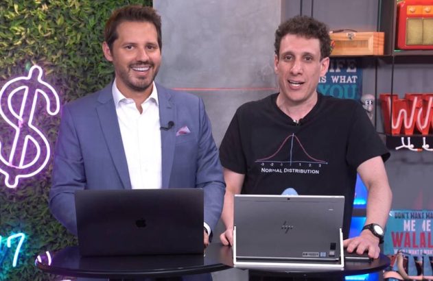 Dois homens sorriem em estúdio com notebooks; um de terno, outro com camiseta de distribuição normal.