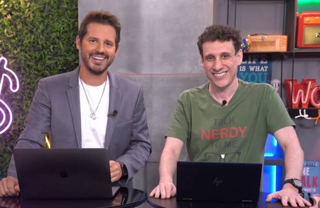 Dois homens sorrindo em estúdio, cada um com um laptop à frente.