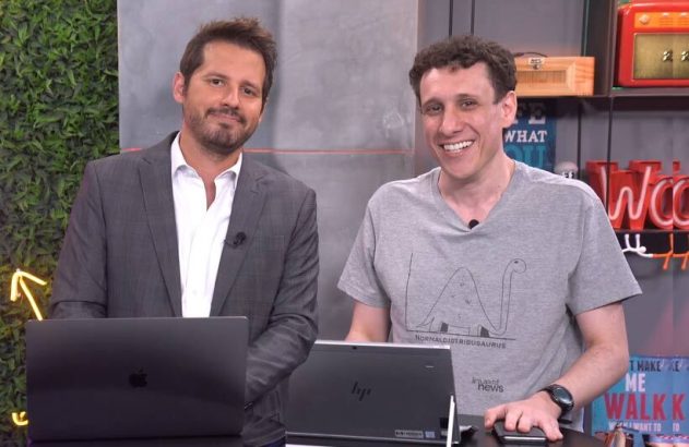 Dois homens sorrindo em um cenário de apresentação com laptops.