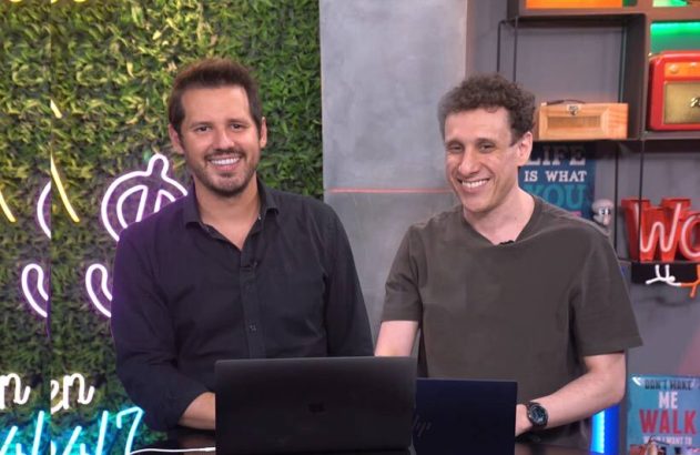 Dois homens sorridentes com laptops em um estúdio.