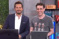 Dois homens sorrindo: um de terno, outro de camiseta, posam com laptops em um estúdio.