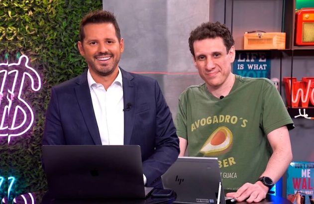 Dois homens em estúdio com laptops na mesa; um sorri para a câmera.