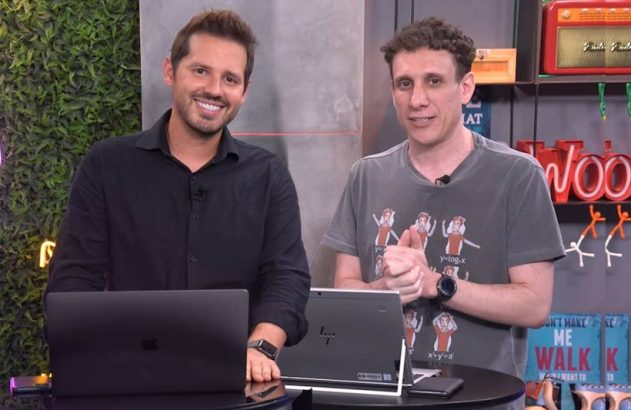 Dois apresentadores em estúdio com laptops. Um sorri e o outro gesticula, em apresentação ou webinar.