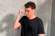 Homem de camiseta preta com dedo na cabeça, fazendo um gesto que sugere "pense" ou "ter uma ideia".