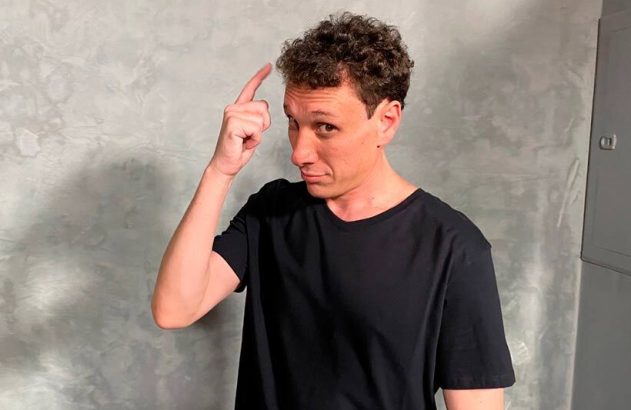 Homem de camiseta preta com dedo na cabeça, fazendo um gesto que sugere "pense" ou "ter uma ideia".