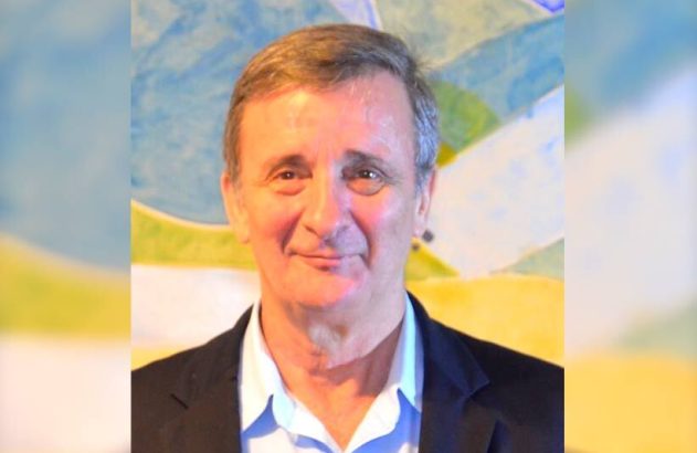 Retrato de homem sorridente de meia-idade, camisa azul e blazer.