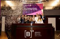 Pessoas comemoram na B3, com confetes caindo sobre o balcão da bolsa de valores.