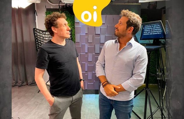 Dois homens em estúdio, olhando para o alto, onde se vê o logo "oi" amarelo.