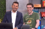 Dois apresentadores sorridentes, um de terno e outro de camiseta, atrás de bancadas com laptops.