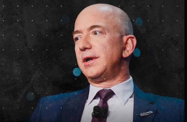 Jeff Bezos, calvo, de terno e gravata, discursando em um evento com fundo escuro.