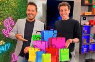Dois homens sorridentes apontam para uma pilha de sacolas de compras coloridas.