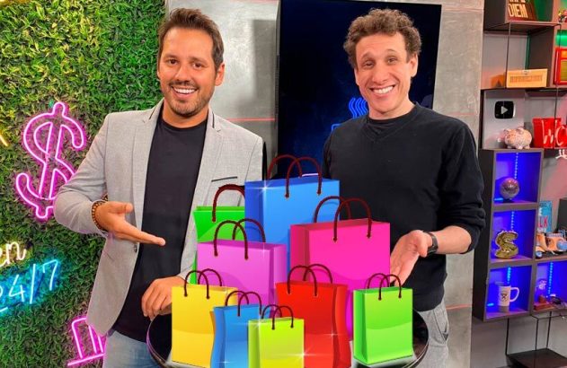 Dois homens sorridentes apontam para uma pilha de sacolas de compras coloridas.