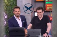 Dois homens sorrindo em estúdio com laptops, um logo de dois peixes acima.