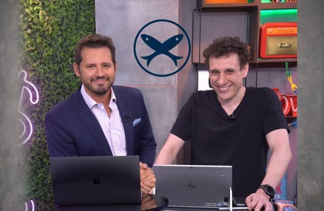 Dois homens sorrindo em estúdio com laptops, um logo de dois peixes acima.