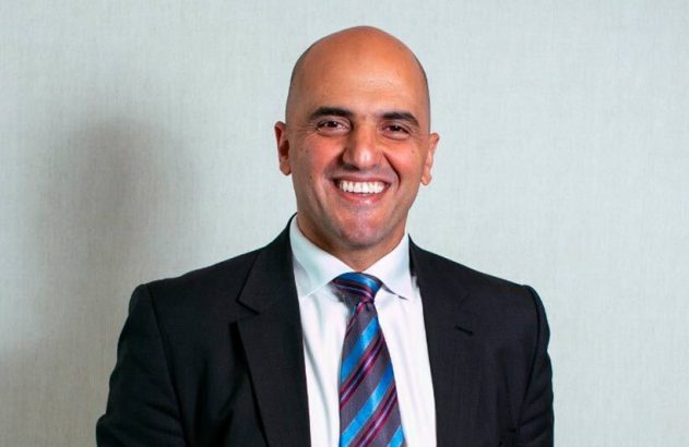 Retrato profissional de um homem careca sorridente, de terno e gravata.