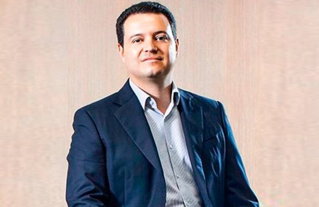 Homem sorridente de paletó azul e camisa listrada, olhando para frente.