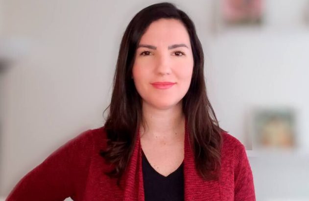 Mulher de cabelo escuro e casaco vinho, sorrindo para a câmera.