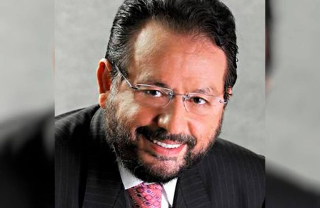 Homem sorridente de óculos, barba e terno.