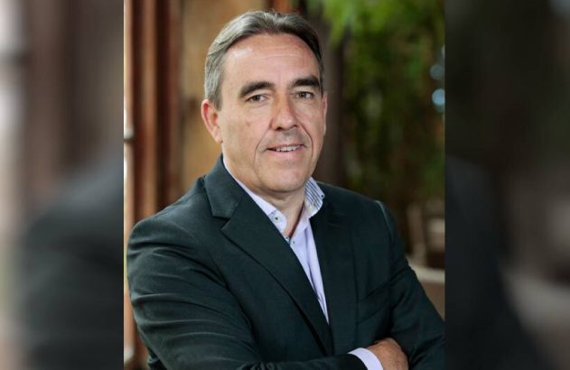 Retrato de homem de terno escuro, camisa clara e braços cruzados, olhando para a câmera.